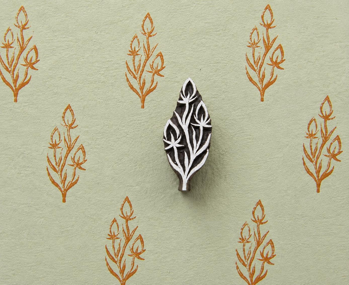 Hand carved botanical sprig wood block stamp with three flower buds, shown on handmade green paper with repeated orange botanical prints