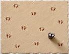 Hand carved little footprint wood stamp shown on natural handmade paper with repeated brown footprint impressions