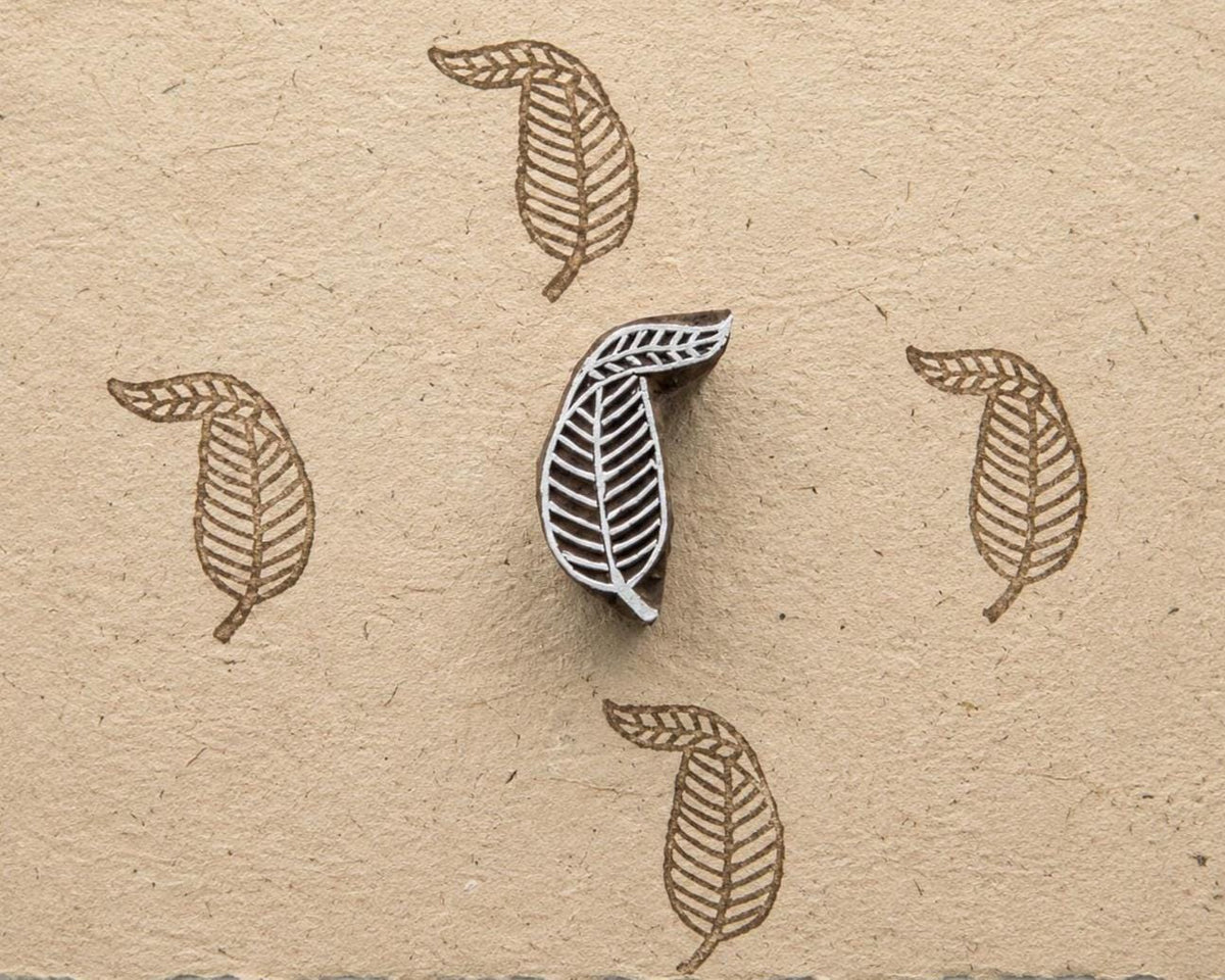 Hand carved leaf wood printing block shown with repeated botanical impressions on handmade paper