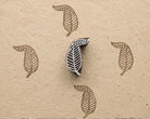 Hand carved leaf wood printing block shown with repeated botanical impressions on handmade paper