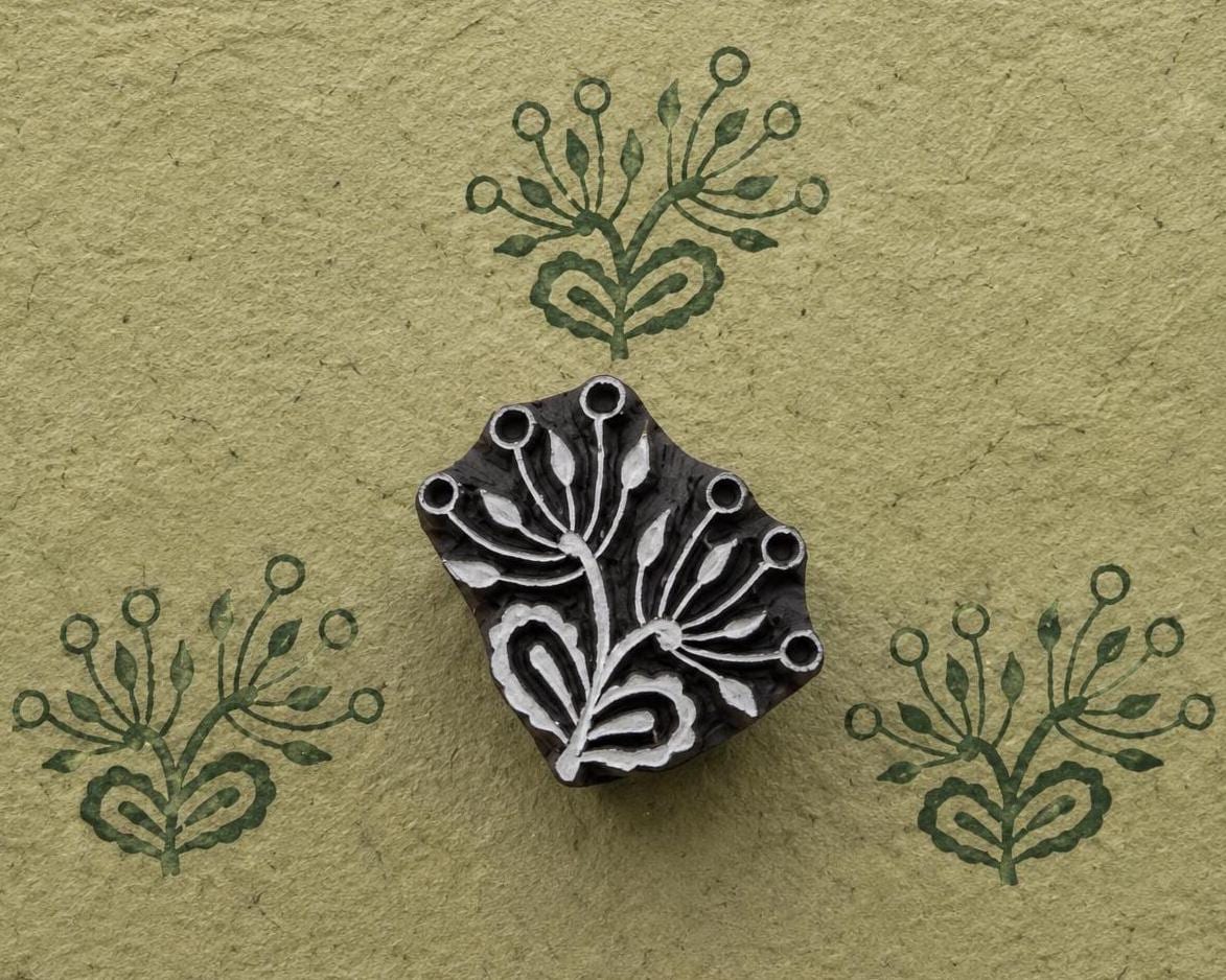 Hand carved botanical sprig wood printing block with repeated green impressions on handmade paper
