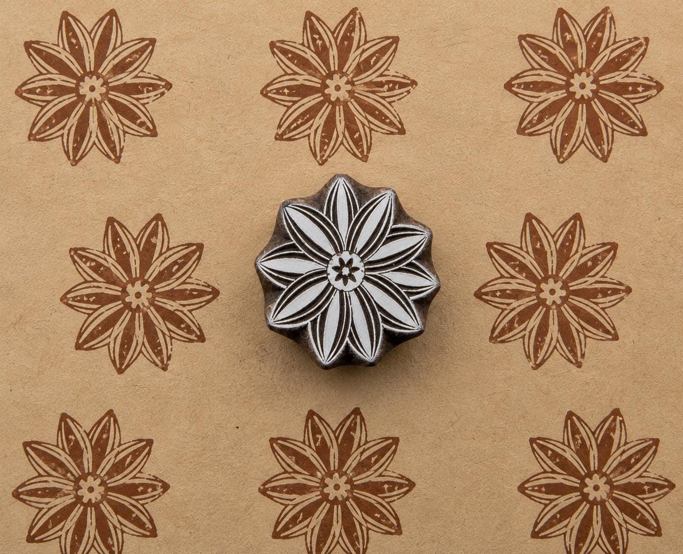 Hand-carved wooden flower printing block shown with repeated brown floral impressions on handmade tan paper.