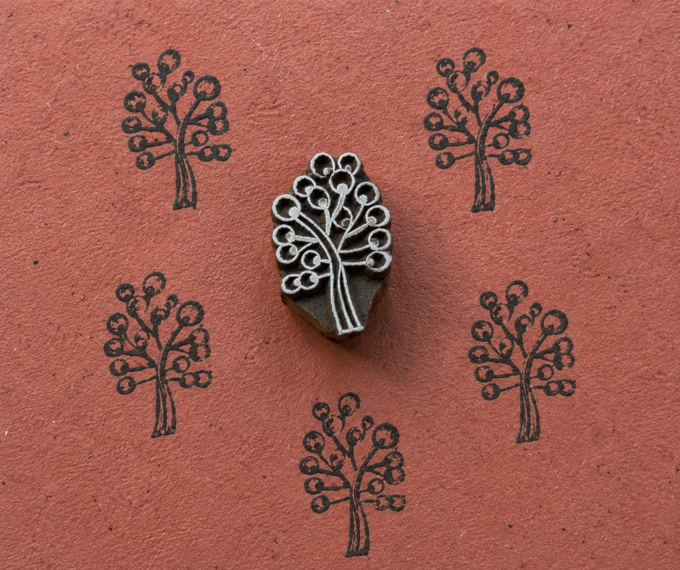 Hand carved wooden Berry Tree stamp shown with repeated dark botanical tree impressions on textured terracotta handmade paper.