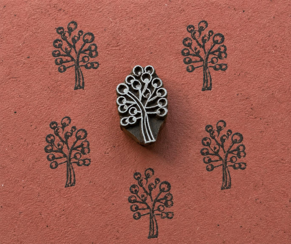 Hand carved wooden Berry Tree stamp shown with repeated dark botanical tree impressions on textured terracotta handmade paper.