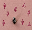 Hand-carved tiny wooden stamp featuring a delicate Berry Blossom Sprig, shown with repeated burgundy impressions on textured handmade pink paper.