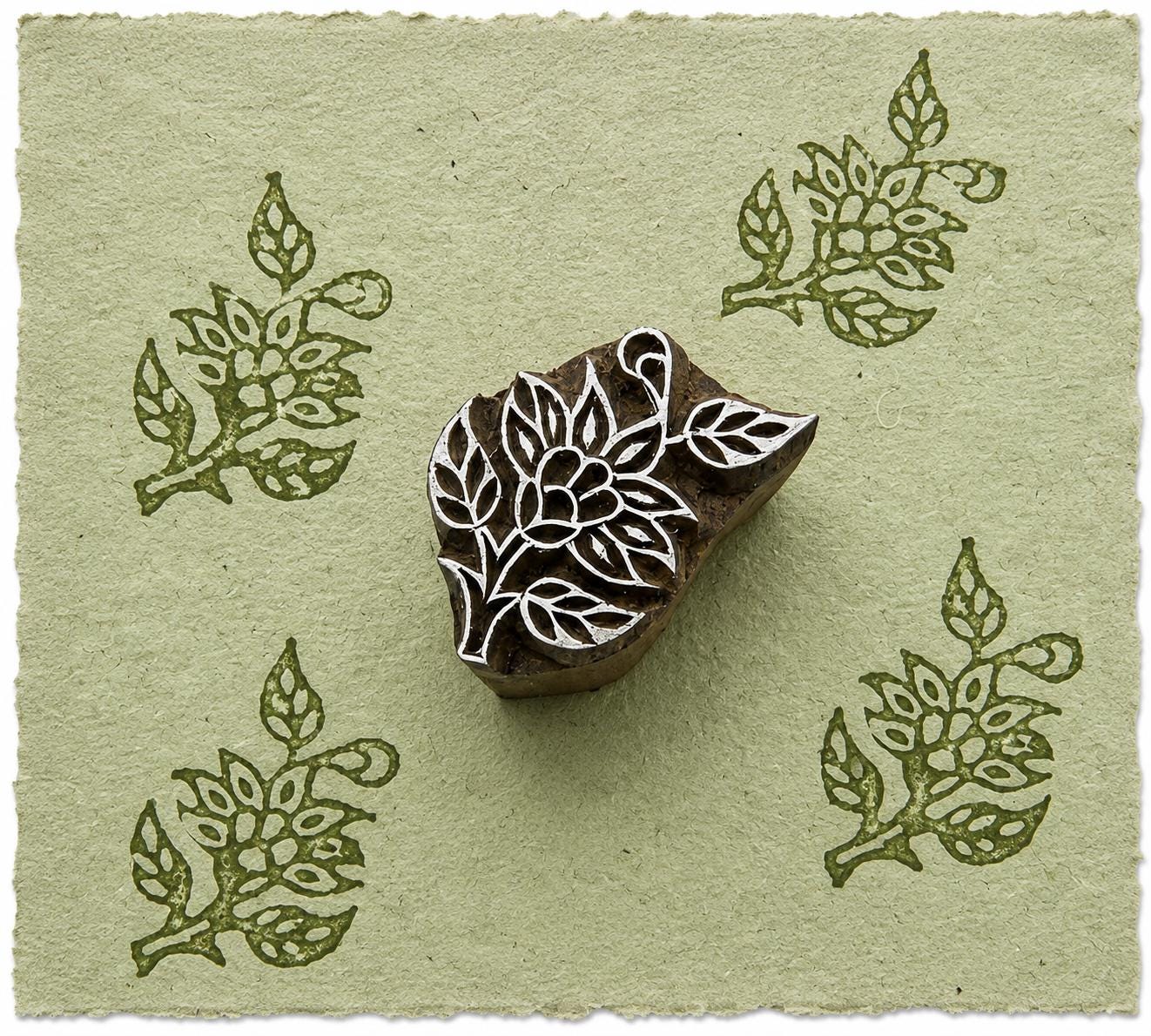 Hand carved botanical leaf wood printing block with repeated floral leaf impressions on handmade sage green paper