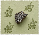 Hand carved botanical leaf wood printing block with repeated floral leaf impressions on handmade sage green paper