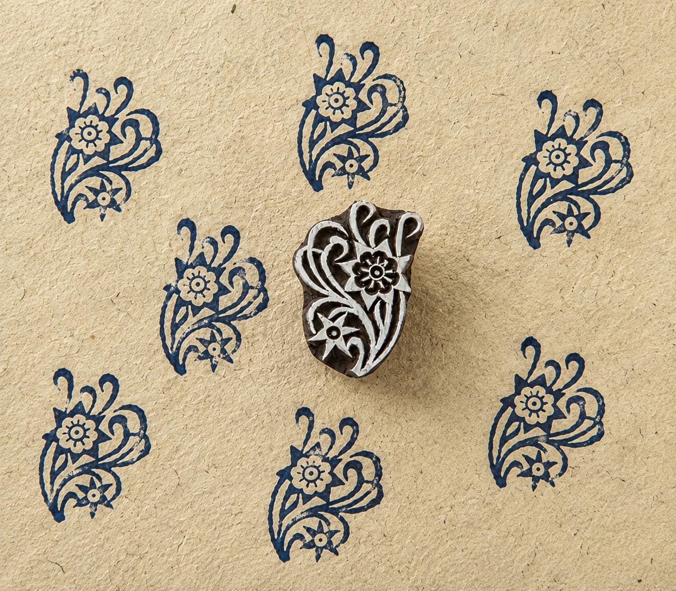 Hand-carved wooden block with a paisley floral design, shown with repeated navy impressions on textured handmade paper.