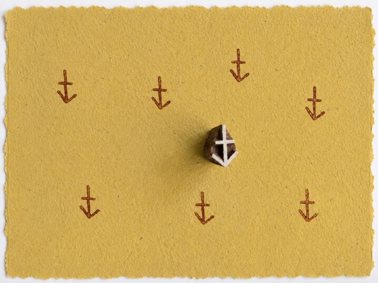 Tiny Sagittarius zodiac symbol stamped repeatedly on yellow handmade paper with wooden printing block