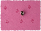 Tiny Cancer zodiac symbol stamped repeatedly on pink handmade paper with wooden printing block