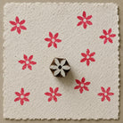 Hand carved six-petal folk flower wooden printing block with repeated red impressions on handmade paper