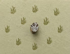 A delicate botanical motif inspired by a small tuft of wild grass, hand carved into wood with fine, organic lines and tiny dot details.