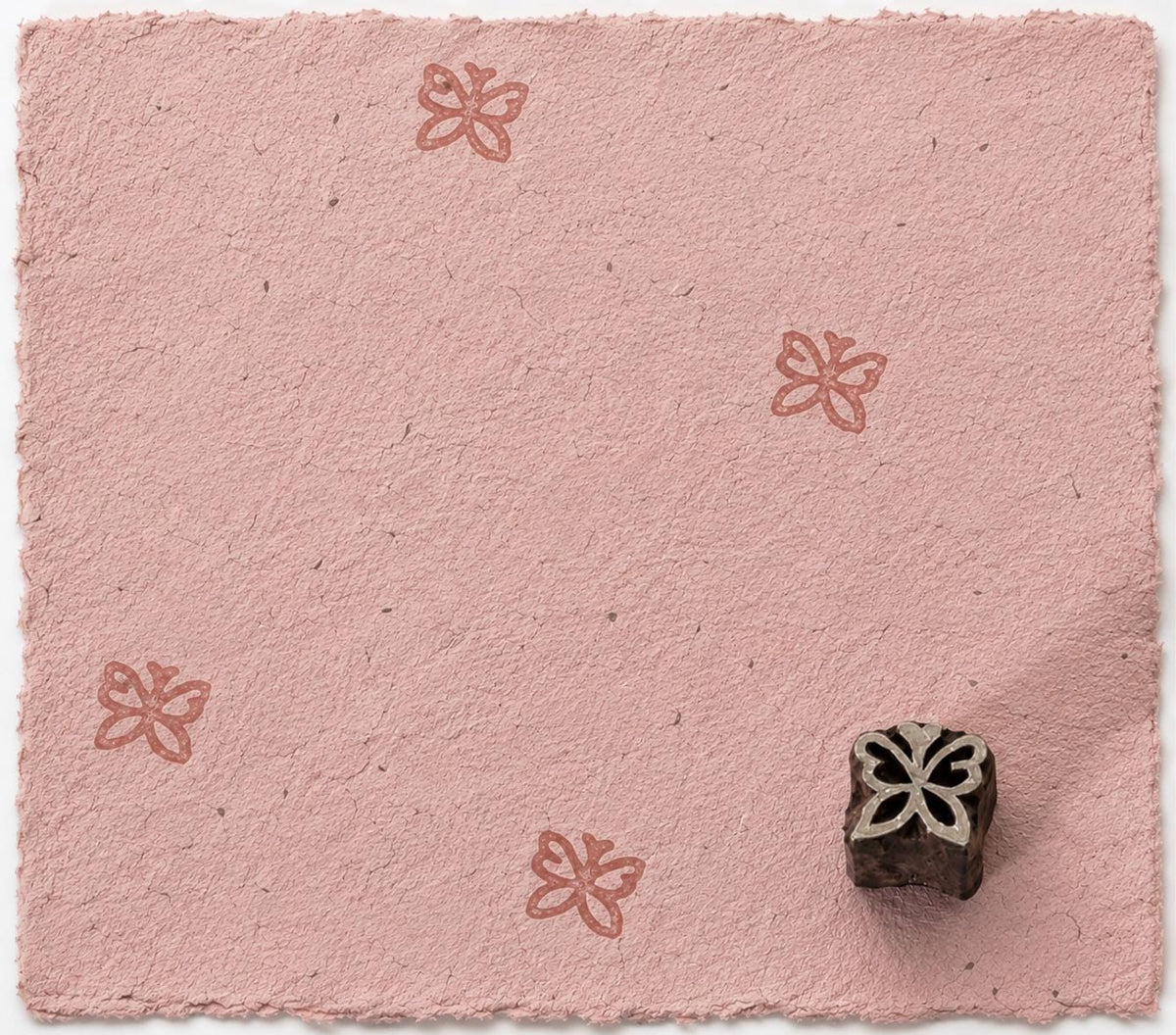 Hand carved Tiny Garden Butterfly wood stamp with repeated butterfly impressions on pink handmade paper.