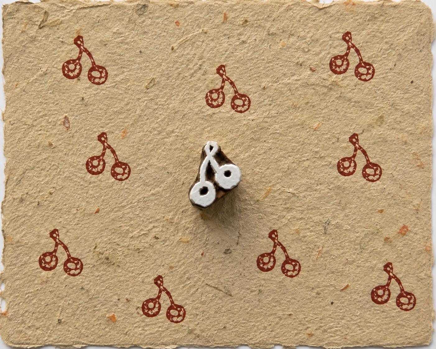 Tiny hand carved cherry pair wooden printing block stamped in red pink ink on textured handmade paper for fabric printing, journaling, and craft projects.
