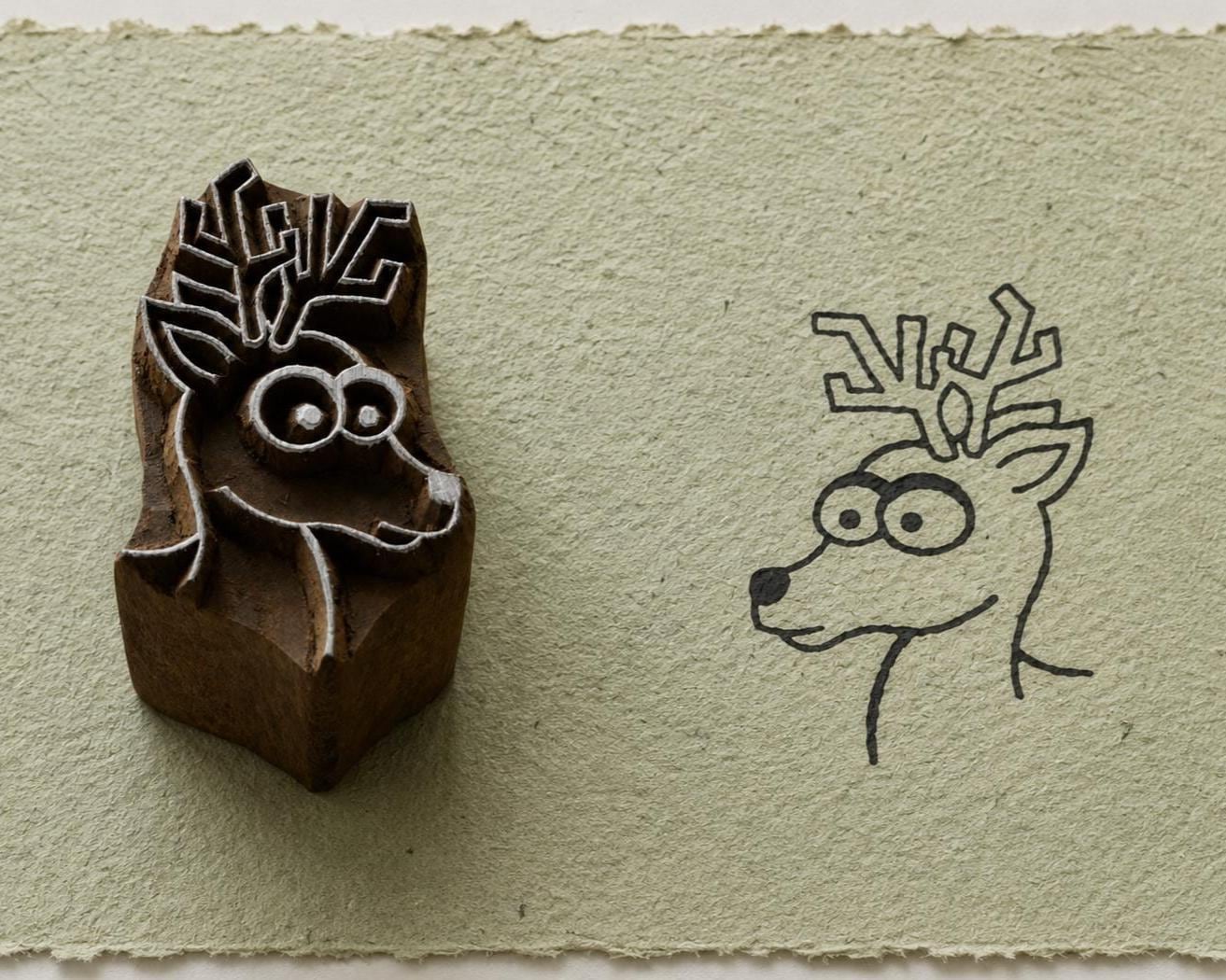 Hand carved whimsical reindeer wooden printing block beside its printed reindeer impression on handmade paper