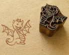 Hand carved whimsical baby dragon wooden printing block shown beside its printed dragon impression on handmade textured paper