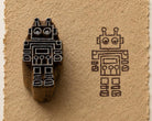 Hand carved wooden robot printing block shown beside its robot print impression on textured handmade paper