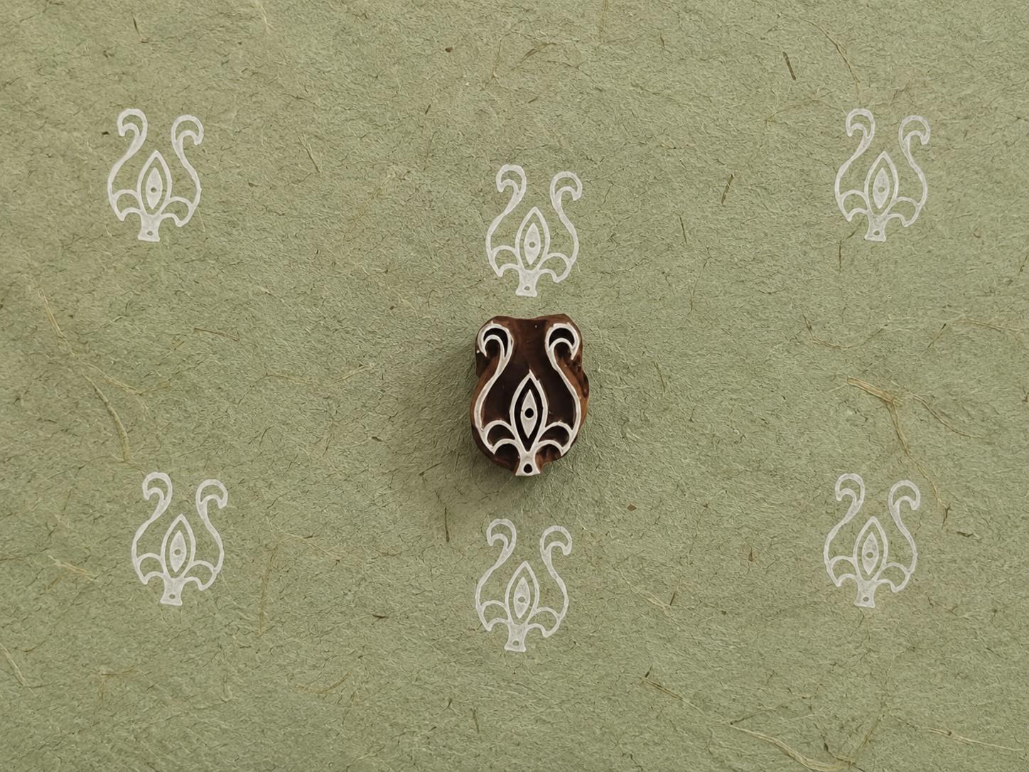 Hand carved wooden printing block with an ornamental botanical motif surrounded by repeated white prints on textured handmade paper