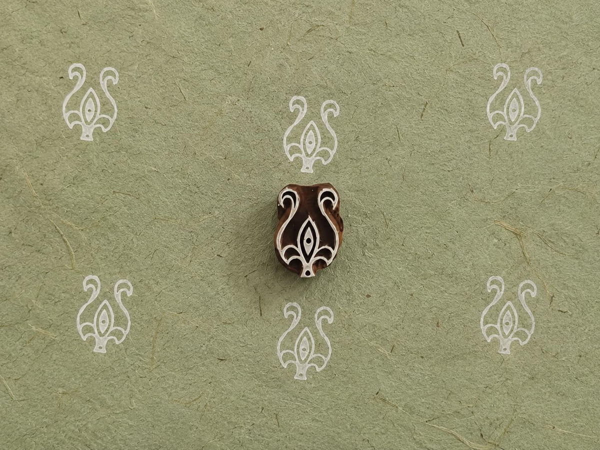 Hand carved wooden printing block with an ornamental botanical motif surrounded by repeated white prints on textured handmade paper