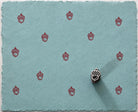 Tiny hand carved Indian wood printing block with acorn motif, shown with repeated red impressions on blue handmade paper