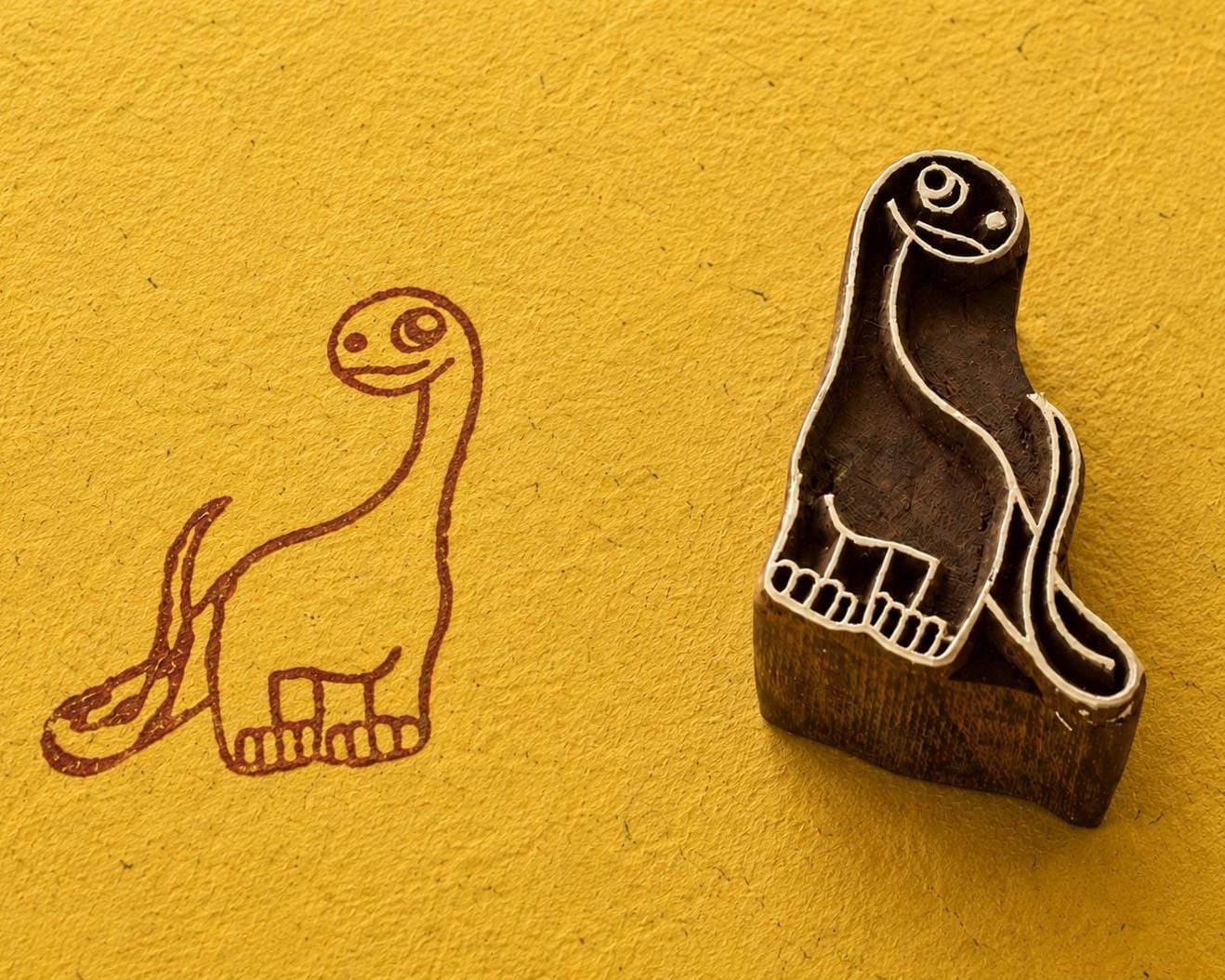 Hand carved Happy Brontosaurus wooden printing block shown beside its dinosaur print on textured yellow handmade paper