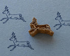 Hand carved Leaping Deer wooden printing block with repeated leaping deer impressions on textured blue handmade paper