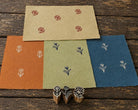 Set of three hand carved Indian wooden printing blocks with different floral designs and hand printed flower patterns on coloured handmade paper.
