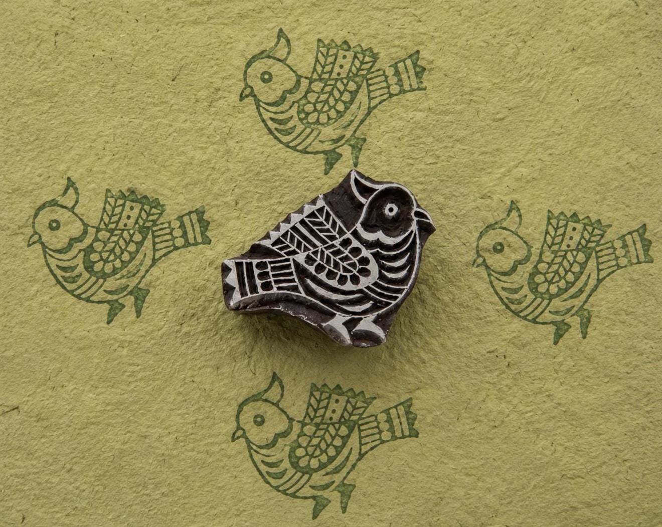 Carved decorative bird woodblock with repeating green bird prints on handmade paper