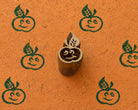 Hand carved wooden smiling apple printing block surrounded by six dark green apple prints on textured orange handmade paper.