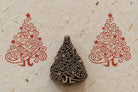 Hand carved wooden Christmas tree printing block with swirling branches and stars, shown between two red printed impressions on textured handmade paper.