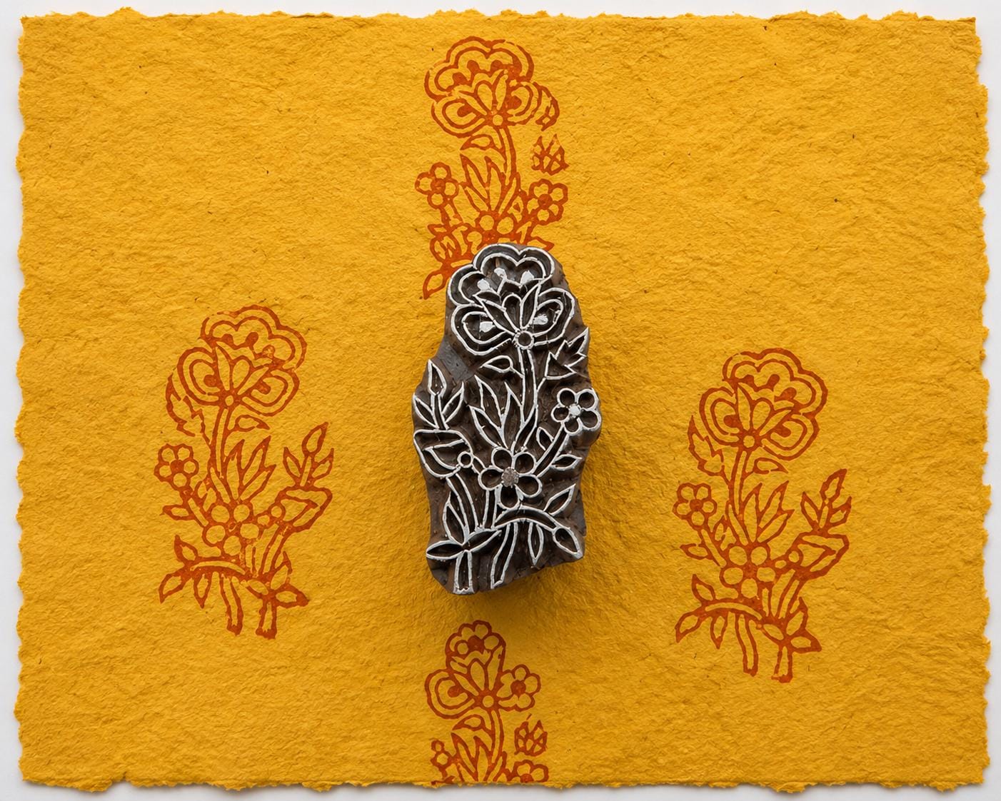 Hand carved floral bouquet wood printing block shown on golden handmade paper with repeated botanical impressions