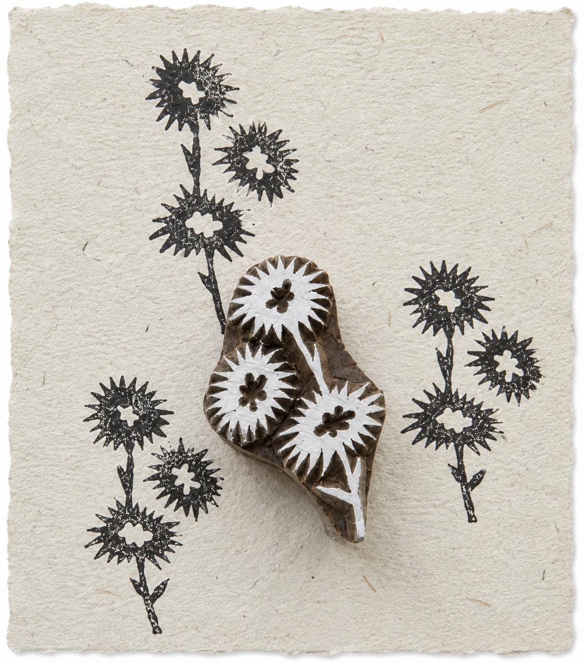 Hand carved spiky wildflower wood printing block shown on handmade ivory paper with repeated black botanical impressions