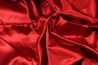 Close-up of deep crimson faux silk satin fabric with a smooth surface, soft folds and beautiful sheen.