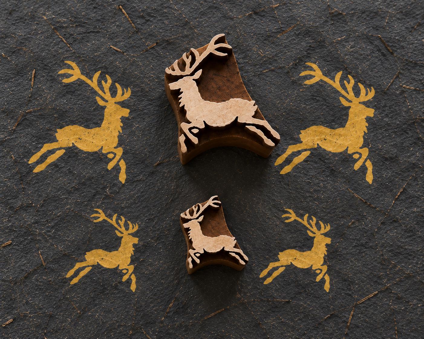 Set of two hand carved leaping reindeer wooden printing blocks with golden deer impressions on a dark textured background