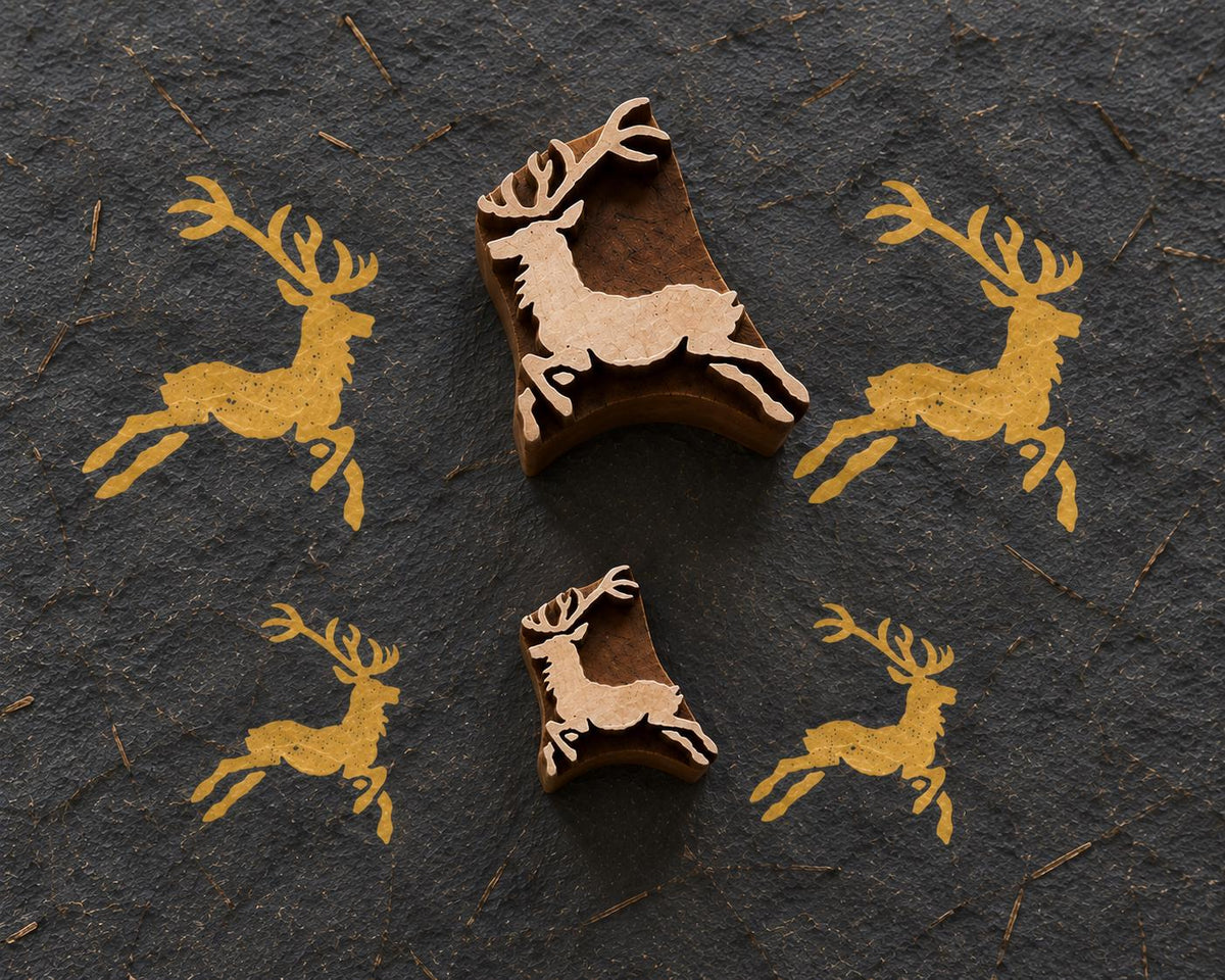 Set of two hand carved leaping reindeer wooden printing blocks with golden deer impressions on a dark textured background