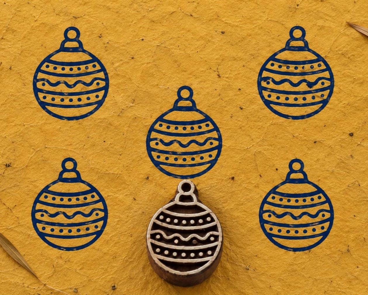 Hand carved festive Christmas ornament wooden printing block surrounded by navy blue ornament prints on textured mustard yellow handmade paper