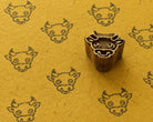 Hand carved wooden baby cow face printing block surrounded by repeated cow face prints on textured golden yellow handmade paper.