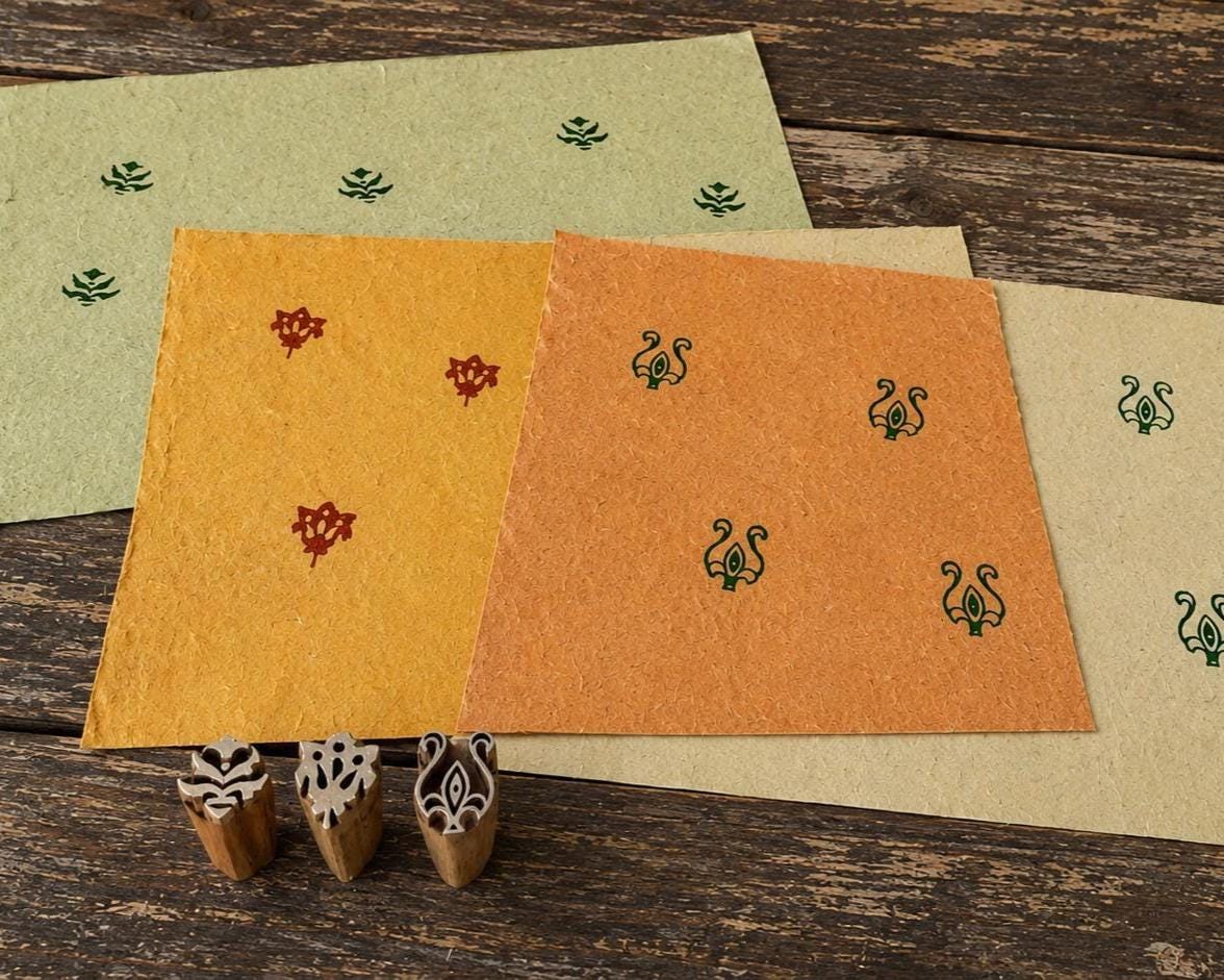 Three small hand-carved Indian motif wooden printing blocks displayed with their printed impressions on colourful handmade paper.