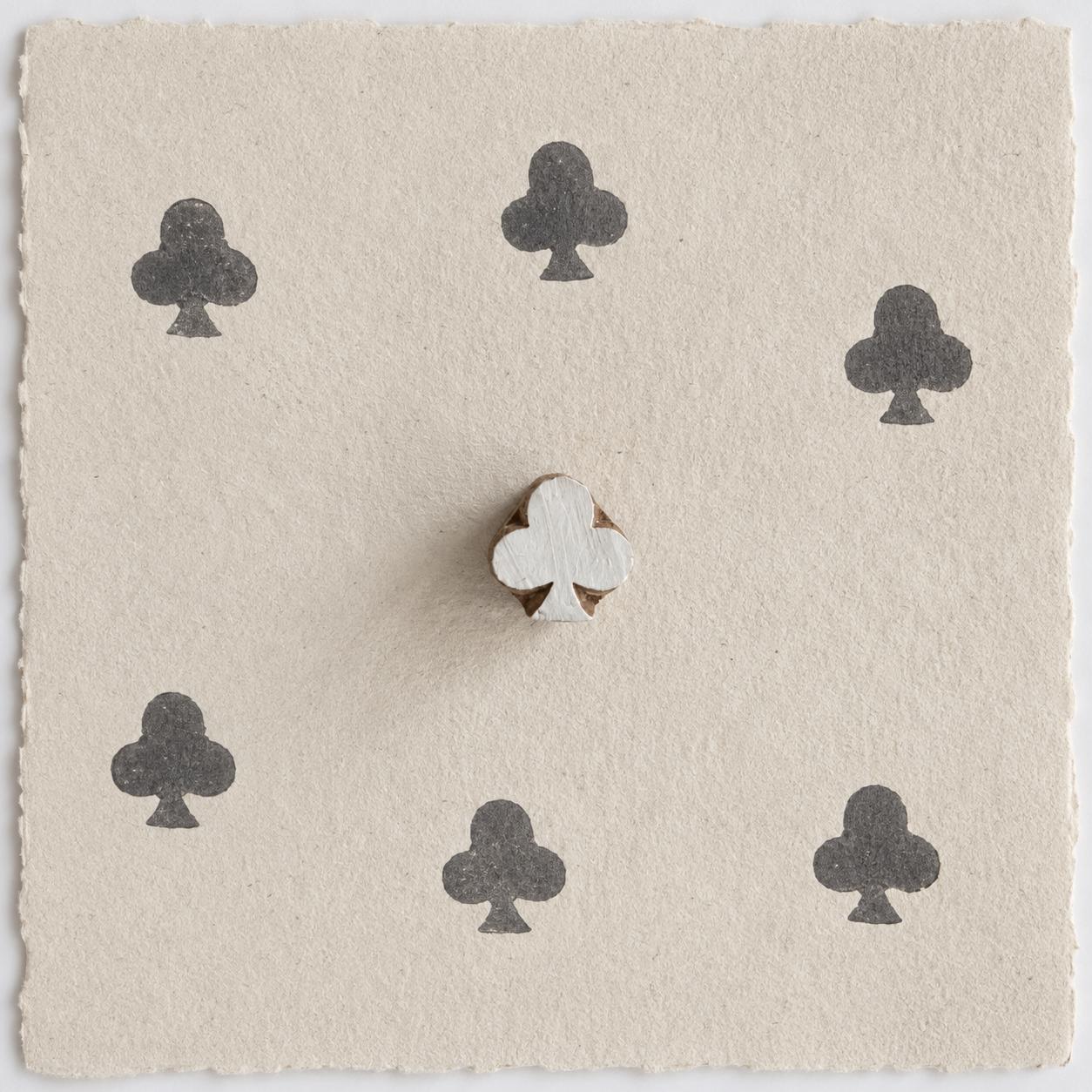 Hand carved wooden club clover printing block shown on handmade paper with six dark ink impressions in a repeating pattern.