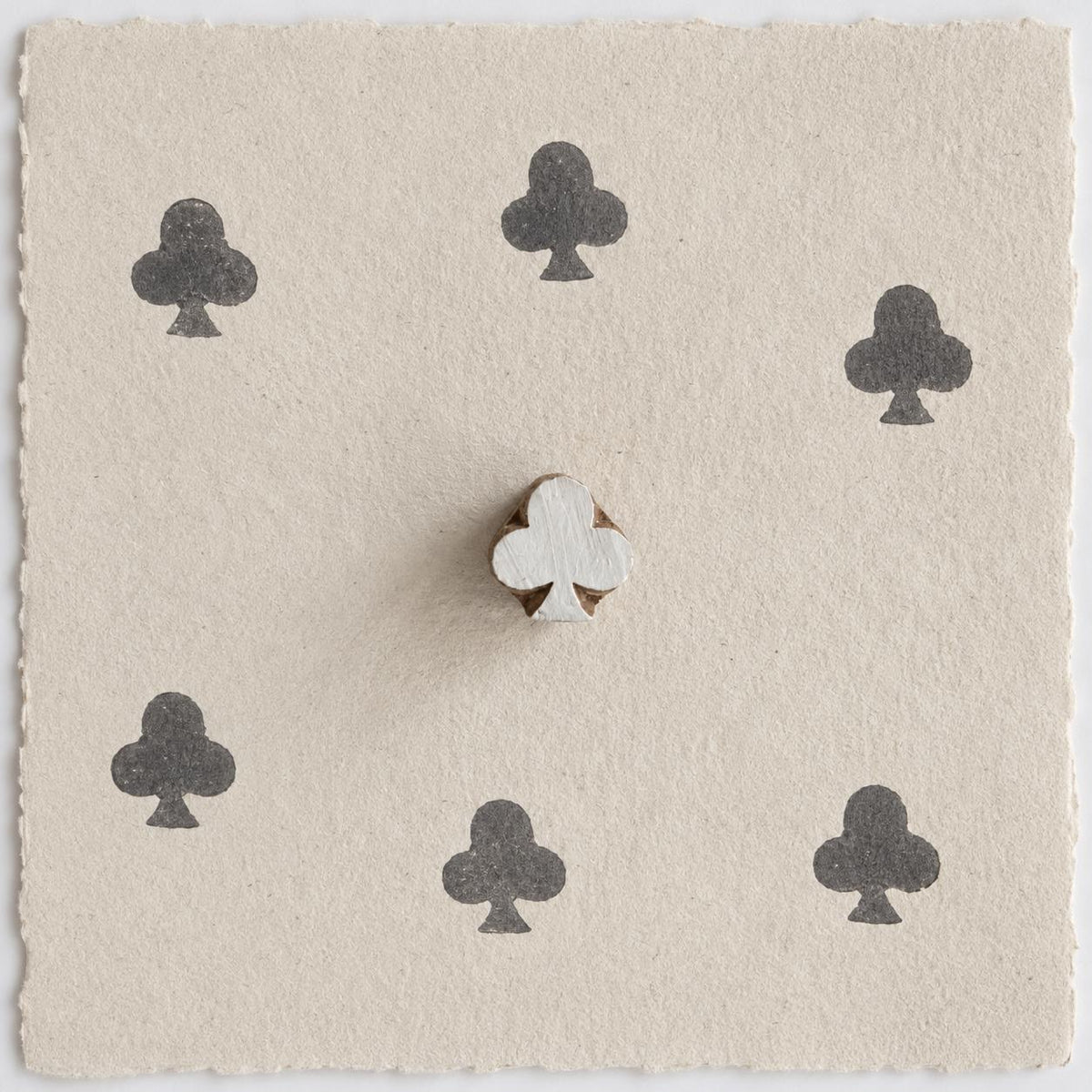 Hand carved wooden club clover printing block shown on handmade paper with six dark ink impressions in a repeating pattern.