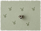 Tiny Taurus zodiac symbol stamped on sage green handmade paper showing the delicate curved zodiac glyph