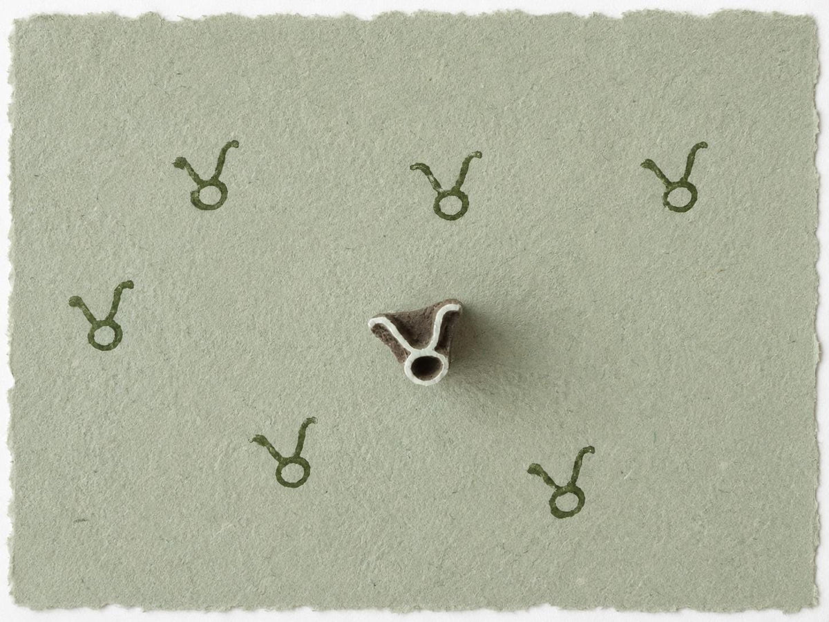 Tiny Taurus zodiac symbol stamped on sage green handmade paper showing the delicate curved zodiac glyph