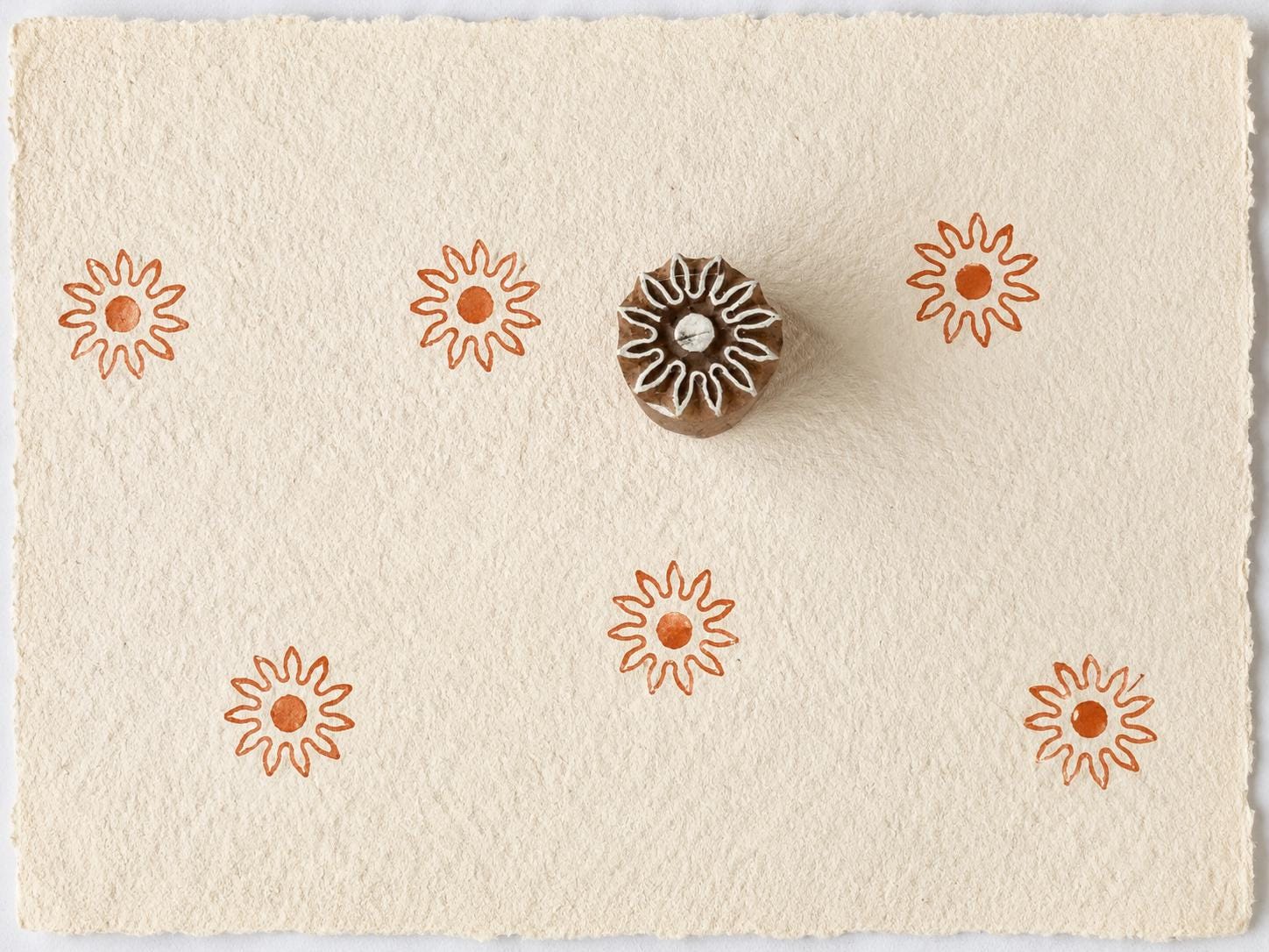 Tiny hand carved sunburst wooden printing block with repeated sun impressions on handmade paper