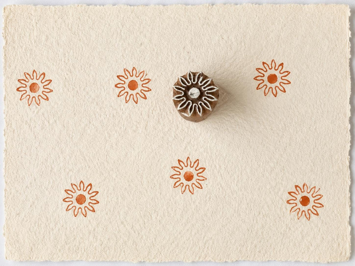 Tiny hand carved sunburst wooden printing block with repeated sun impressions on handmade paper