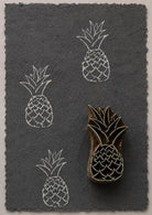 Hand carved tropical pineapple wooden printing block with repeated white impressions on dark handmade paper