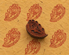 Hand carved Indian wooden printing block with an ornamental floral paisley design, shown beside repeated red prints on handmade paper.