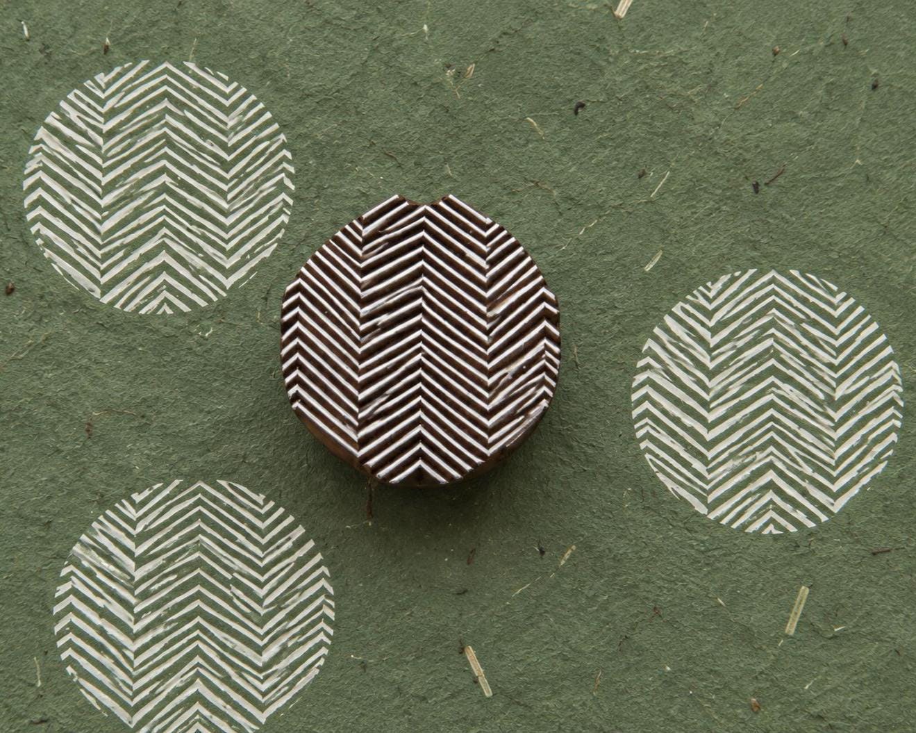 Hand carved Indian wooden printing block featuring a rounded geometric chevron pattern, shown beside repeated white impressions on handmade green paper.