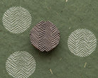 Hand carved Indian wooden printing block featuring a rounded geometric chevron pattern, shown beside repeated white impressions on handmade green paper.