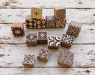Set of 15 hand carved Indian wooden printing blocks with geometric, floral and decorative designs arranged on a distressed white wooden surface