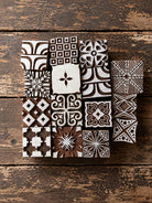Set of 15 hand carved Indian wooden printing blocks with geometric, floral and decorative designs arranged in a group on a wooden surface